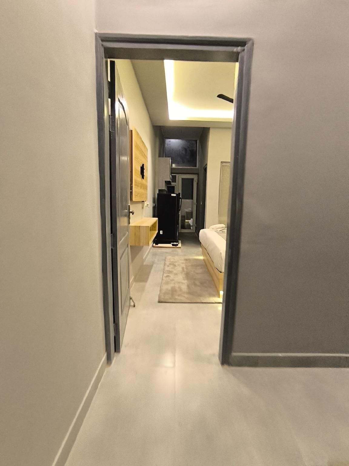 A narrow hallway leading to a bedroom with a bed, a nightstand, and a mirror.