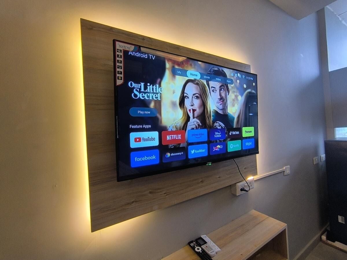 A flat-screen TV mounted on a wall with a wooden panel, displaying a streaming service interface with various app icons.