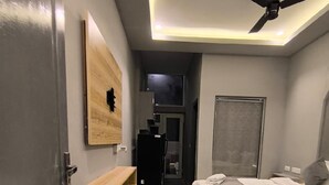 Quarto com cama, ventoinha no teto, prateleira de madeira e uma porta.