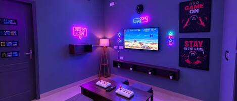Una habitación con espacio de juegos que incluye televisión, consola y letrero de neón.