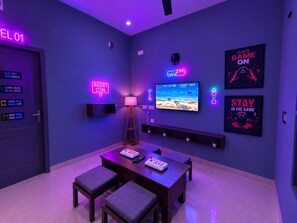 A room with a gaming setup including a TV, gaming console, and a neon sign.