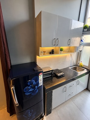 A compact kitchen with a refrigerator, a coffee machine, and a sink.