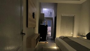 Um corredor estreito que dá para um quarto com cama, ventilador de teto e uma porta.