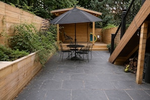 Eine Terrasse mit Tisch und Stühlen, ein Holzzaun und eine hölzerne Konstruktion mit Dach.