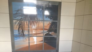 A bathroom with a toilet, a window with a view of palm trees, and a toilet paper holder.