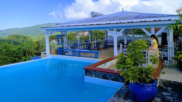 A pool area with a covered seating area, a view of the surrounding landscape, and a clear sky.