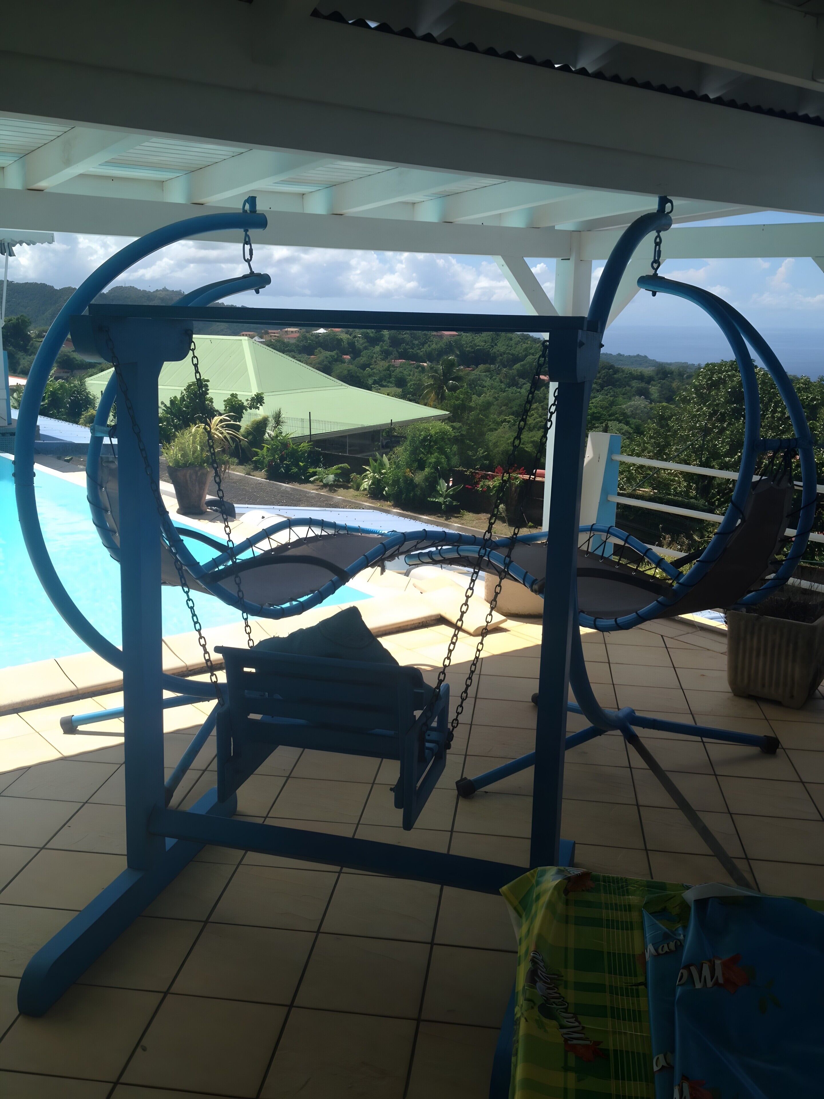 Une balançoire bleue avec vue sur une piscine et une végétation luxuriante.
