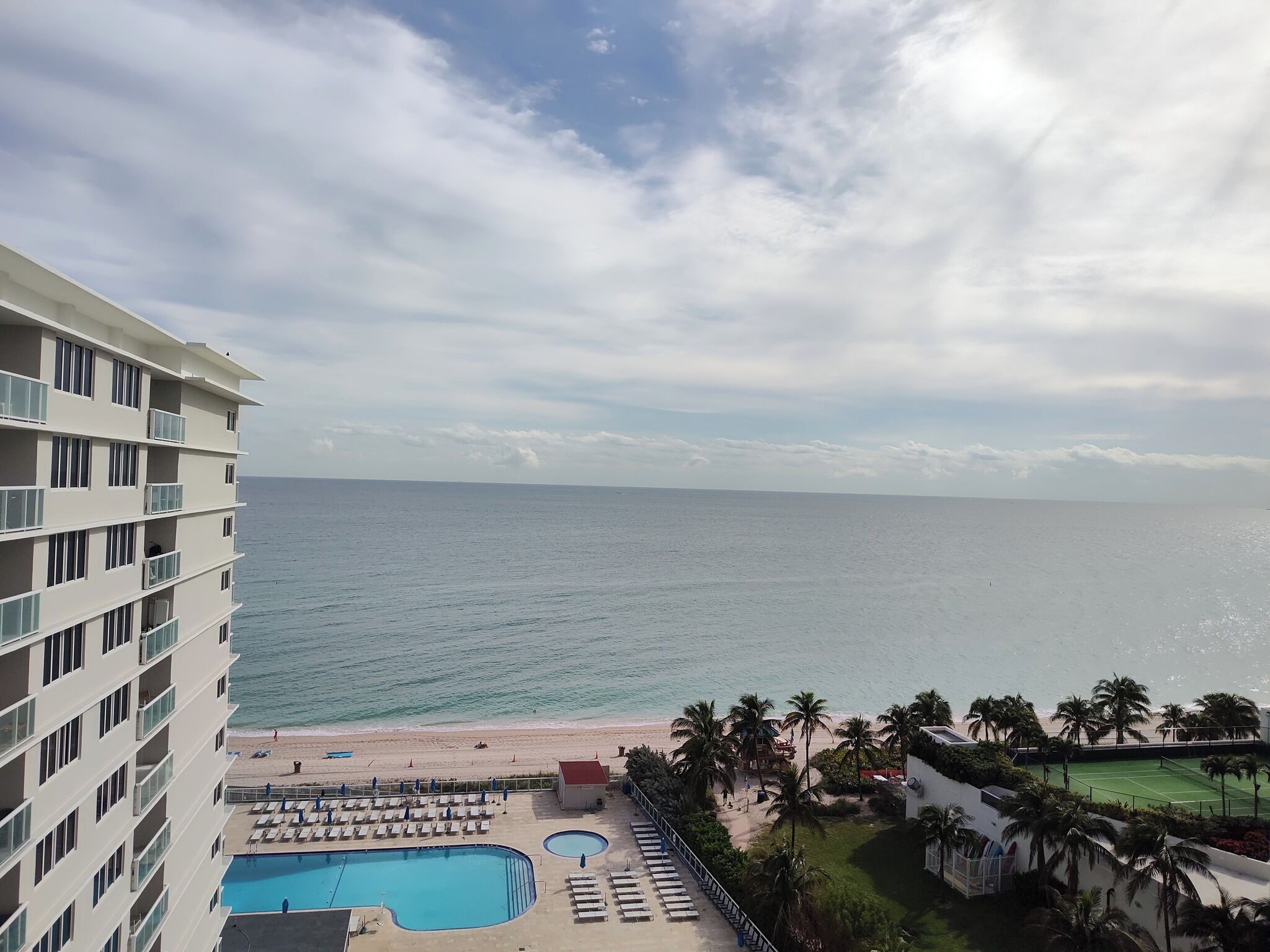 A hotel with a pool, beach, and palm trees.