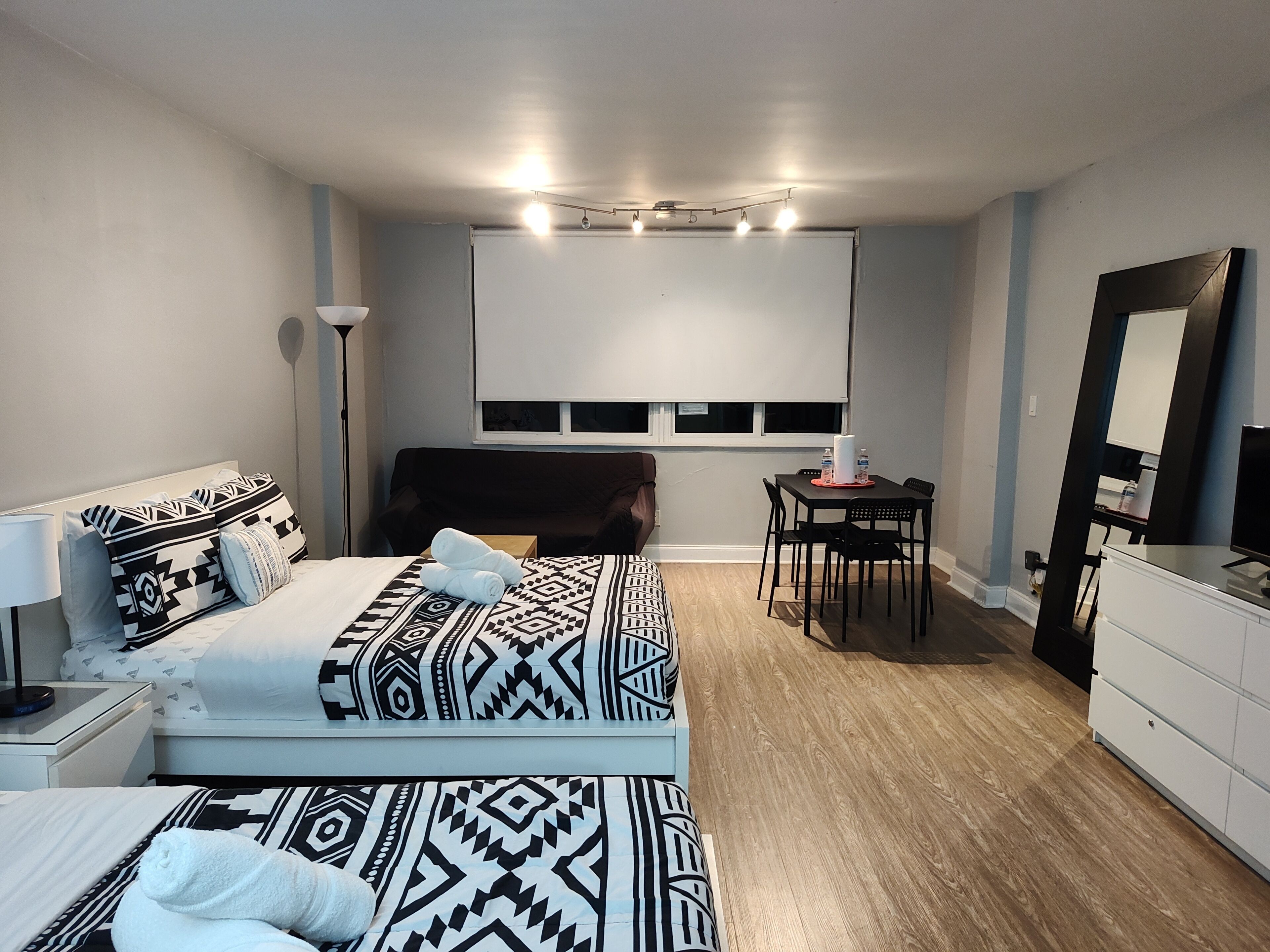 A hotel room with a bed, bedside table, lamp, and a desk with chairs.