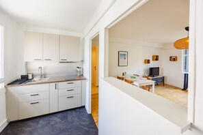 Una cocina moderna con armarios blancos, un lavamanos de acero inoxidable y una zona de comedor con mesa y sillas.