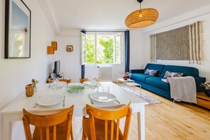 Ein Essbereich mit einem Tisch für vier Personen, einem blauen Sofa und einem großen Fenster mit Blick auf Grünflächen.