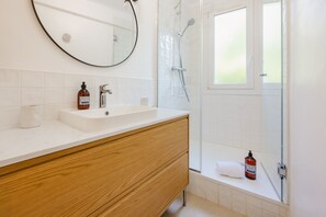 Ein modernes Badezimmer mit einem Holzwaschtisch, einem runden Spiegel, einem weißen Waschbecken und einer Duschkabine aus Glas.