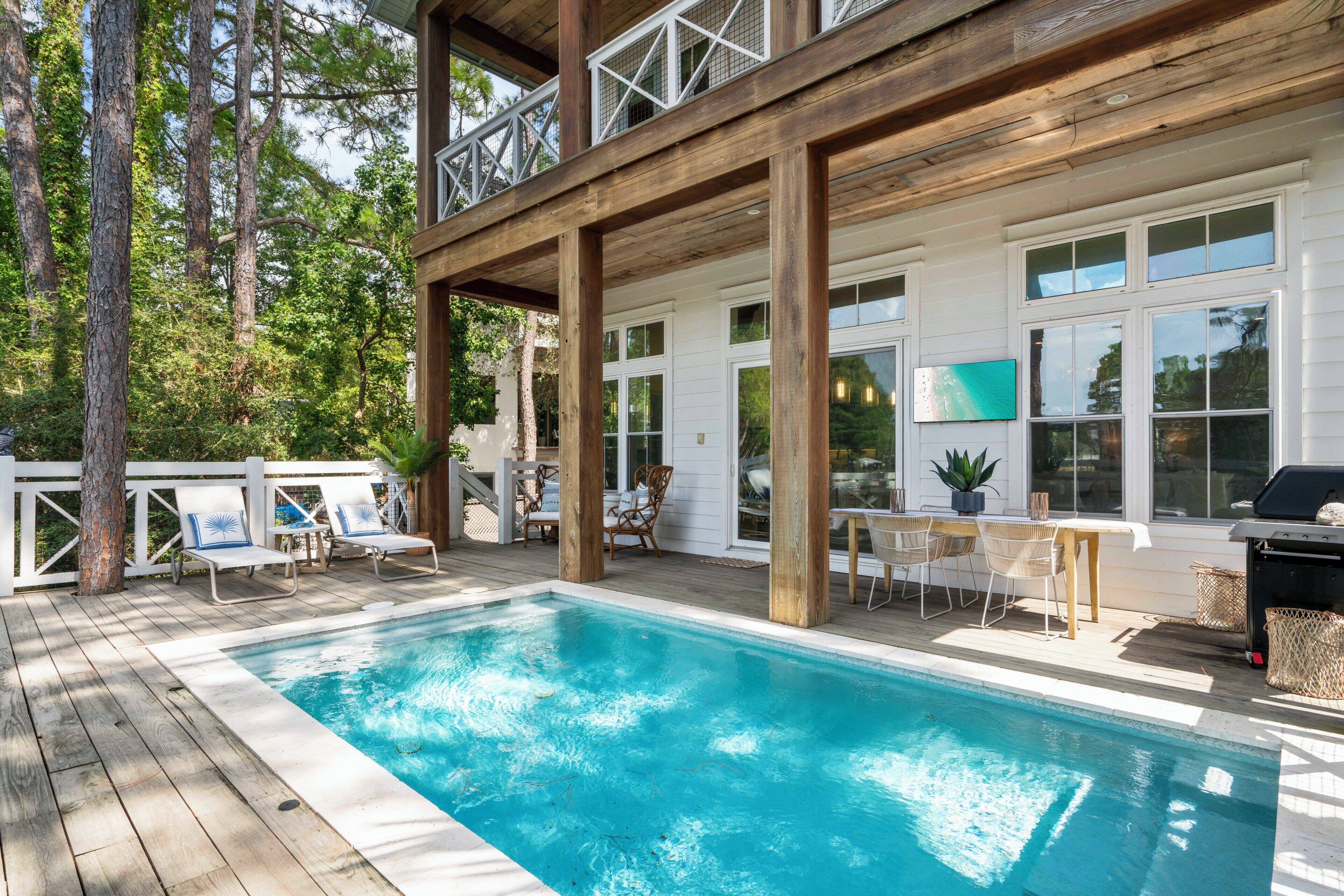 Un espace piscine doté d’une terrasse en bois, de chaises longues et d’une table à manger.