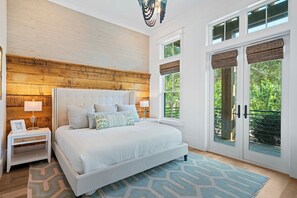 A bedroom with a large bed, two bedside tables, a wooden headboard, and a view of greenery through the windows. - Luxury on Eastern Lake | Lakefront | Private Pool | 6 Beach Bikes (Santa Rosa Beach)