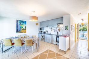 A modern kitchen with a dining area, a large painting, and a view to the outside. - Capsea - Vue sur le port (Capbreton)
