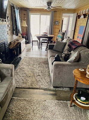 Een woonkamer met een bank, salontafel, open haard en een eethoek met tafel en stoelen.