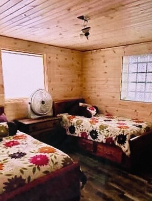 Een blokhut met twee bedden, een ventilator en een raam.