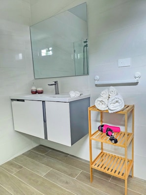 A bathroom with a white vanity, a mirror, a towel rack, and a wooden shelf with towels and a hairdryer. - Laguna Beach 306 Stylish Apartment- Just 3 Minutes Walking to Playa Dominicus (Dominicus)