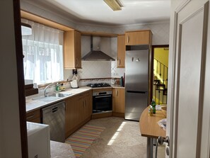 Une cuisine compacte avec des meubles en bois, un réfrigérateur en acier inoxydable, un four encastré et une fenêtre avec des rideaux.