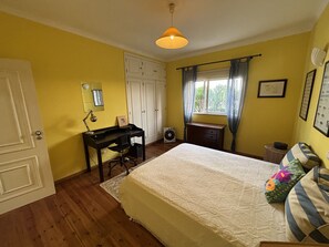 Une chambre à coucher comprenant un lit, un bureau, une armoire et une fenêtre avec des rideaux.