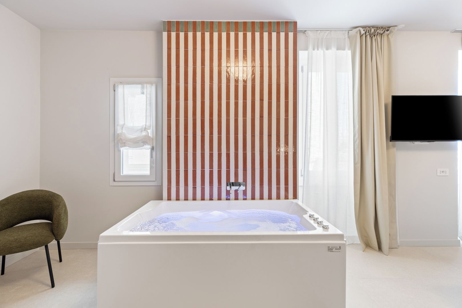 Un baño moderno con bañera, ducha, inodoro, lavabo y televisión montada en la pared.