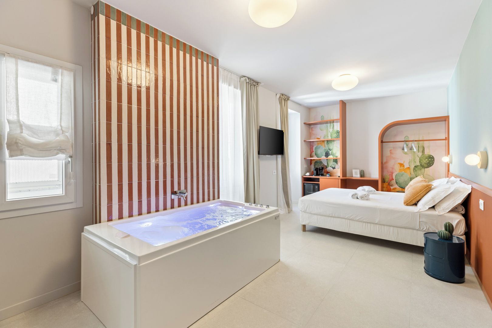 Una camera d'albergo moderna con una vasca, un letto, una televisione e una decorazione a forma di cactus.