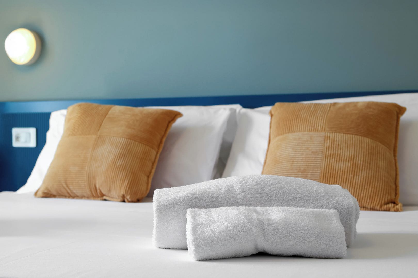 A neatly made bed with white and brown pillows, a white towel, and a blue headboard.