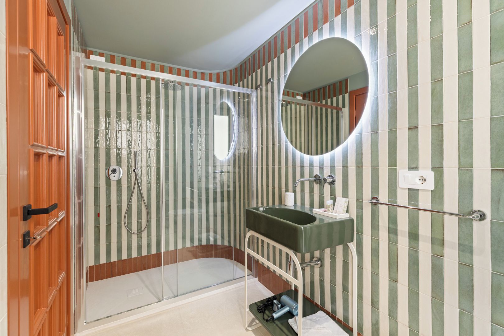 Un bagno con box doccia in vetro, lavabo con specchio e piastrelle a righe sulle pareti.