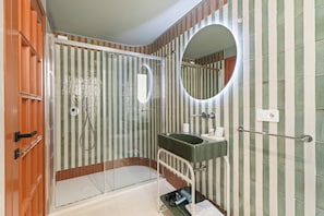 A bathroom with a glass shower enclosure, a sink with a mirror, and striped wall tiles. - Koro guesthouse (Oristano)