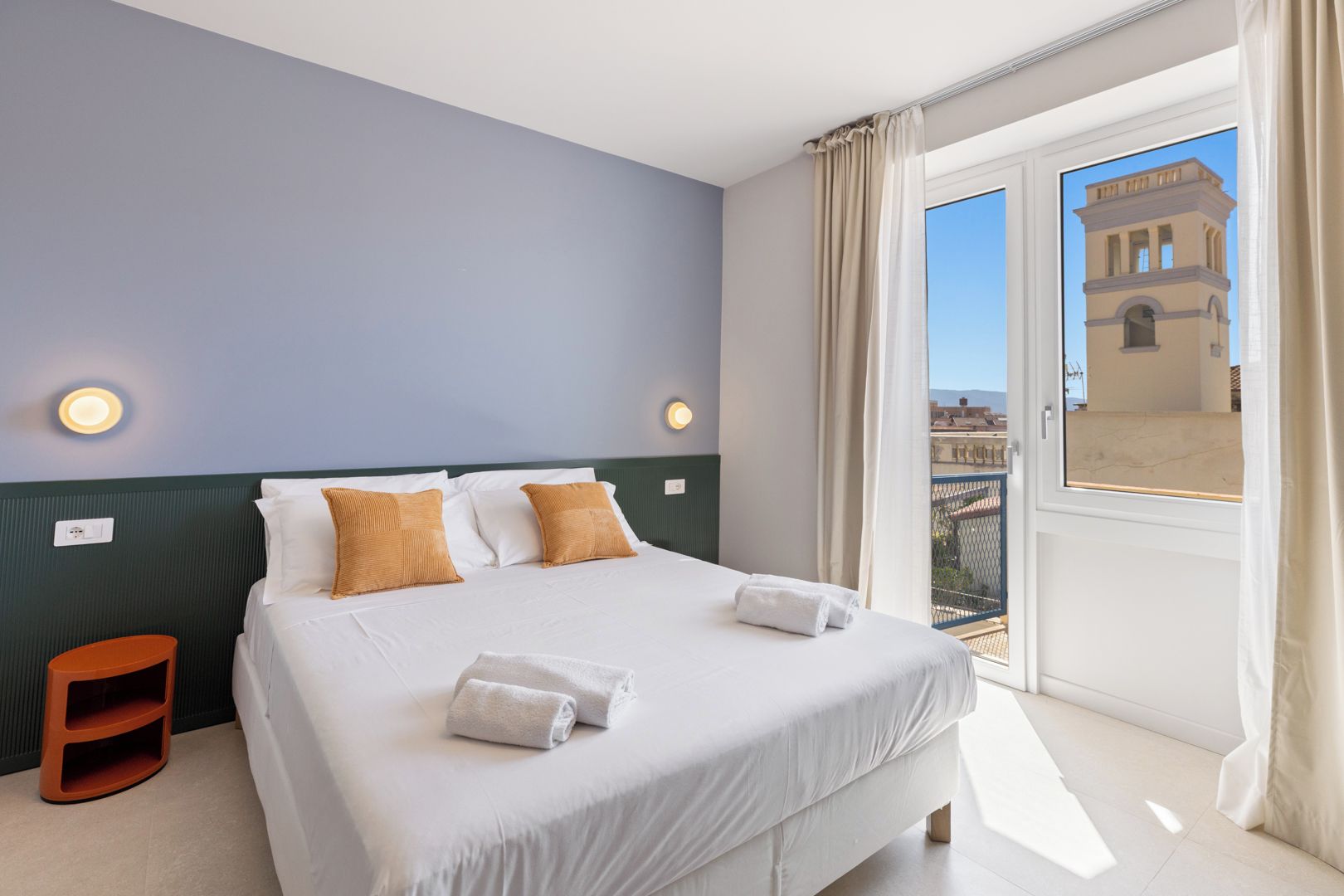 Habitación de hotel con una cama grande, dos almohadas, una mesita de noche y vistas a un edificio a través de una ventana.