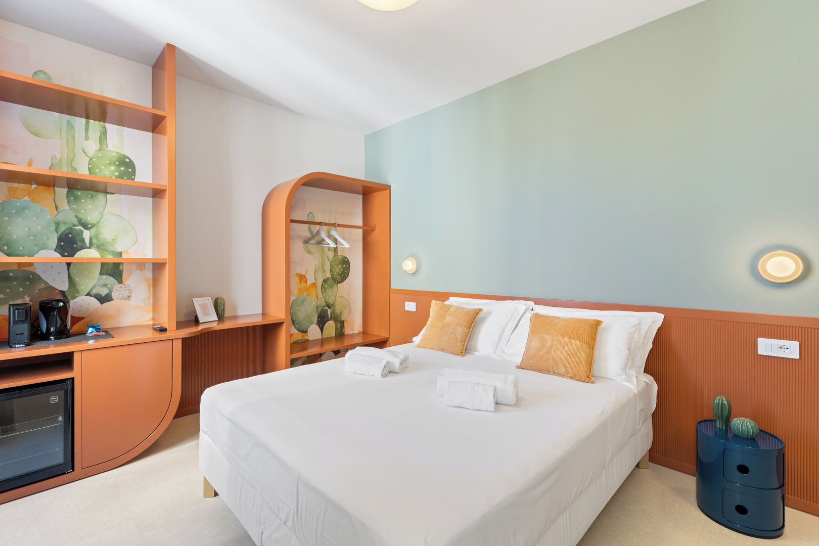 Een hotelkamer met een bed, een bureau met een computer, een koffiezetapparaat en een cactussieraad.