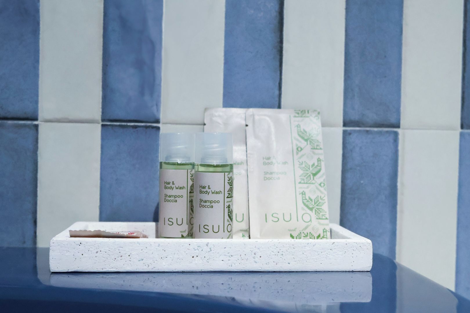A set of toiletries on a white tray against a tiled wall.