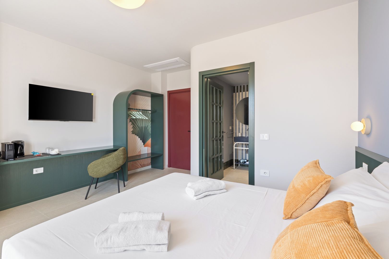 Habitación de hotel con cama, escritorio, silla, televisión y baño visible a través de una puerta abierta.