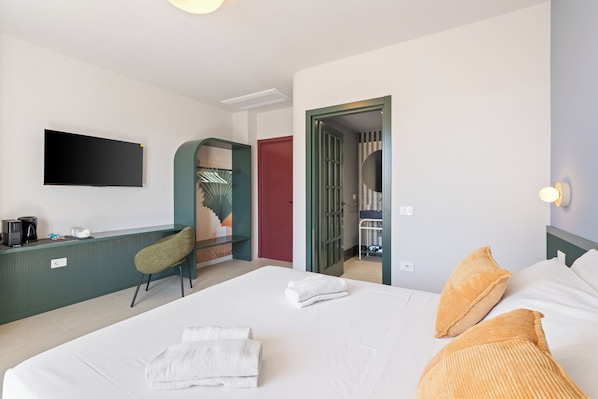 Habitación de hotel con cama, escritorio, silla, televisión y baño visible a través de una puerta abierta.
