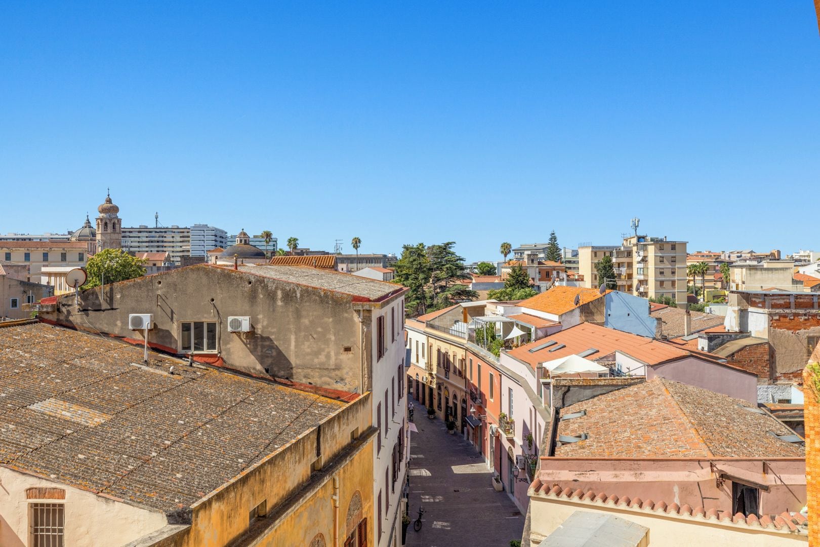 Une rue étroite bordée de bâtiments des deux côtés, un ciel bleu dégagé et une vue lointaine d’une tour.