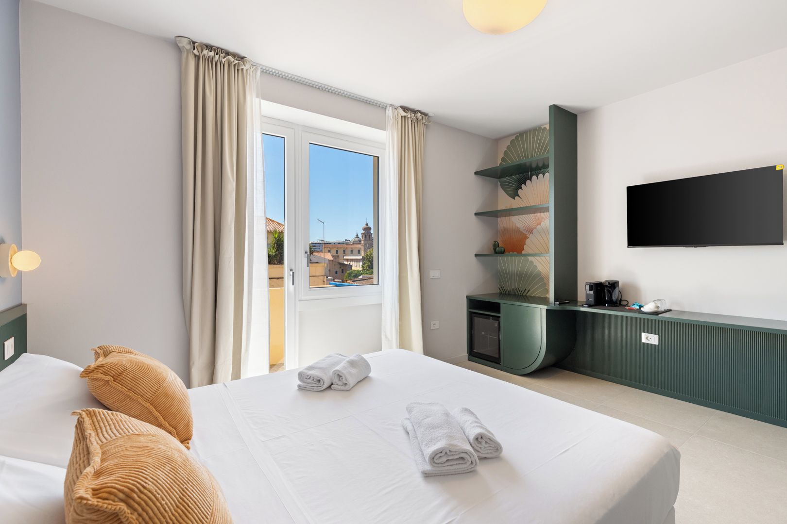 Habitación de hotel con dos camas, un escritorio, un televisor y vista a un edificio.