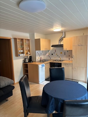 Une cuisine compacte comprenant un coin repas, des meubles en bois, un pare-feu en carrelage et un lave-vaisselle encastré.