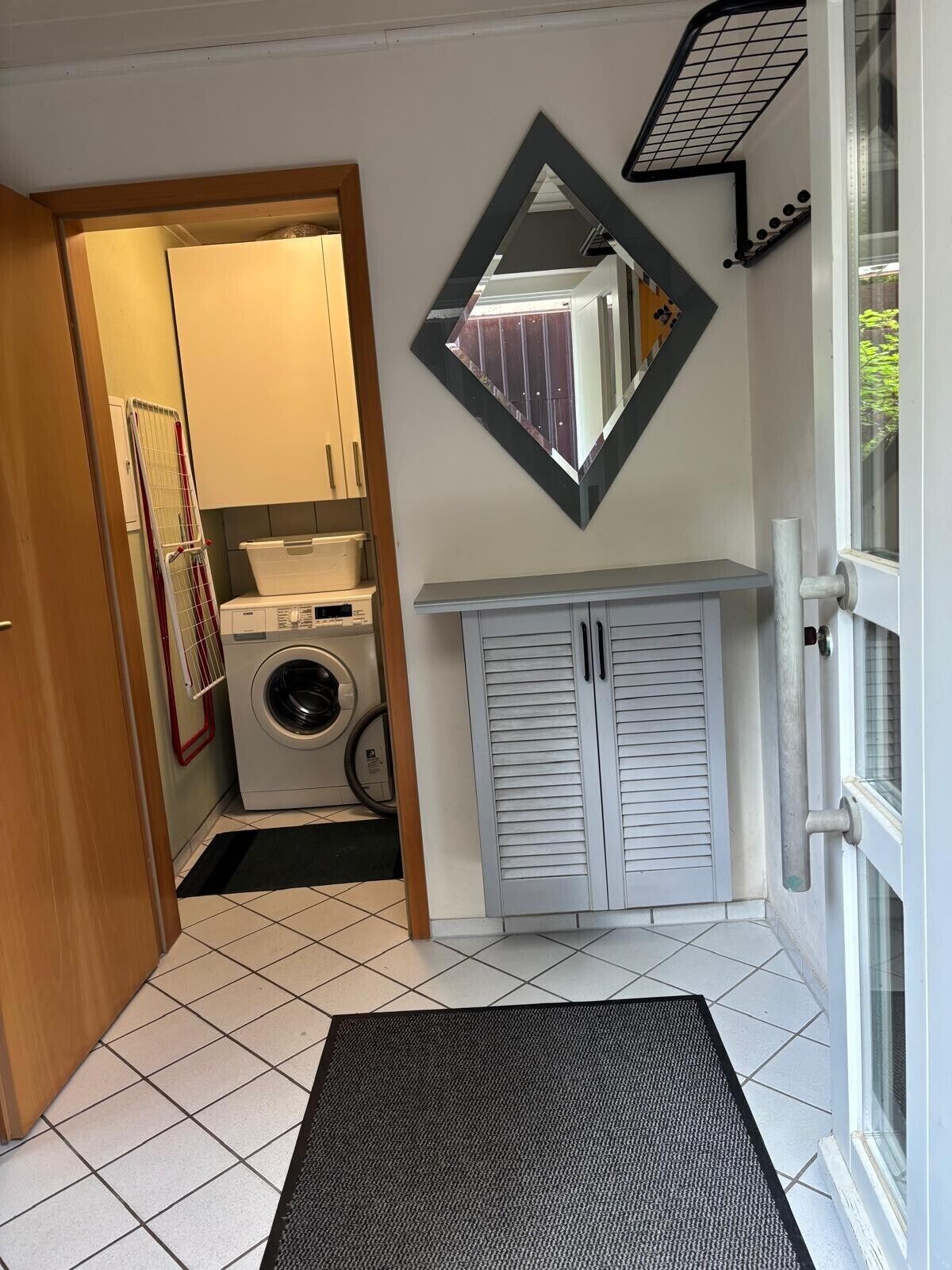 A laundry room with a washing machine, drying rack, and a mirror on the wall.