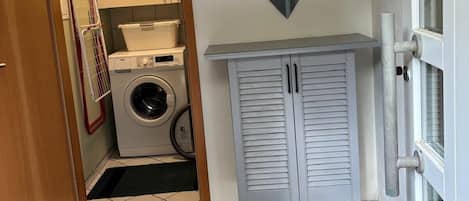 A laundry room with a washing machine, drying rack, and a mirror on the wall.