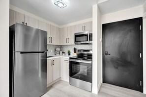 Una cucina moderna con elettrodomestici in acciaio inossidabile, mobili chiari in legno e una porta nera.