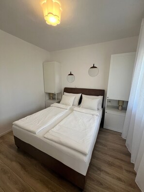 A neatly made bed with white linens in a room with wooden flooring, white walls, and a ceiling light fixture. - Superb 1-bedroom apartment with AC in charming Bibinje 25 meters from Sea (Bibinje)