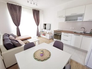 A modern living room with a sofa, a dining table with a placemat, and a kitchen area with cabinets and a microwave. - Superb 1-bedroom apartment with AC in charming Bibinje 25 meters from Sea (Bibinje)