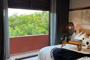 Ein Schlafzimmer mit einem Bett, einem Nachttisch mit Lampe, Blick auf Grünflächen und einer roten Wand.