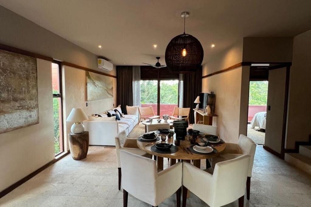 A dining area with a round table, white chairs, and a hanging light fixture.