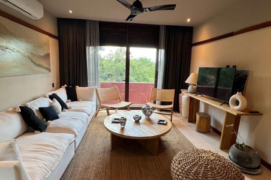 Une chambre d’hôtel avec un canapé, des fauteuils, une table basse, une télévision et un balcon avec des rideaux.