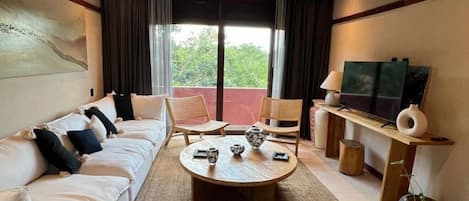 Une chambre d’hôtel avec un canapé, des fauteuils, une table basse, une télévision et un balcon avec des rideaux.