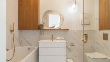 A modern bathroom with a marble vanity, a freestanding bathtub, a toilet, and a glass-enclosed shower area.
