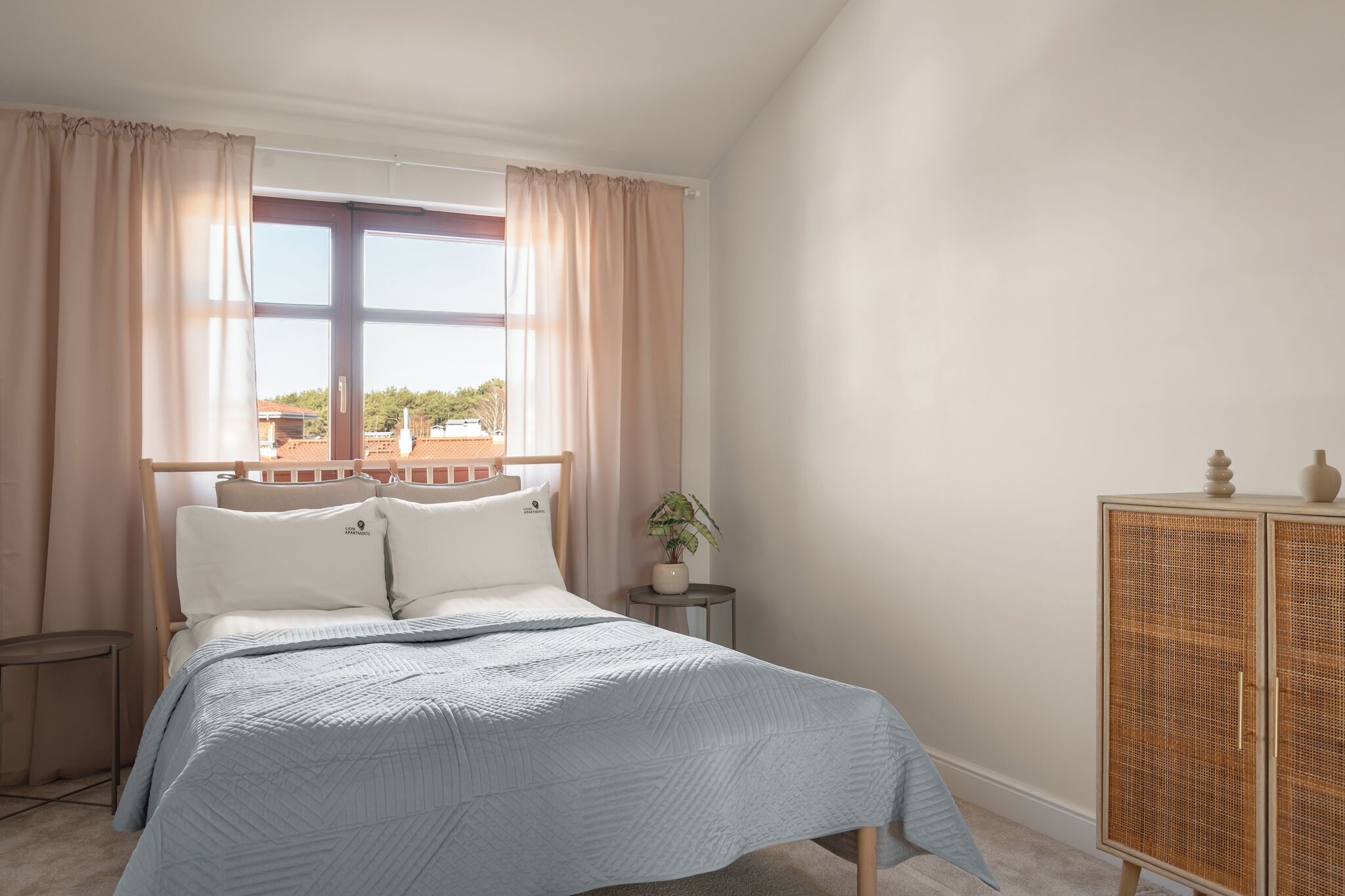 A bedroom with a bed, curtains, a window, a bedside table, a potted plant, and a cabinet.
