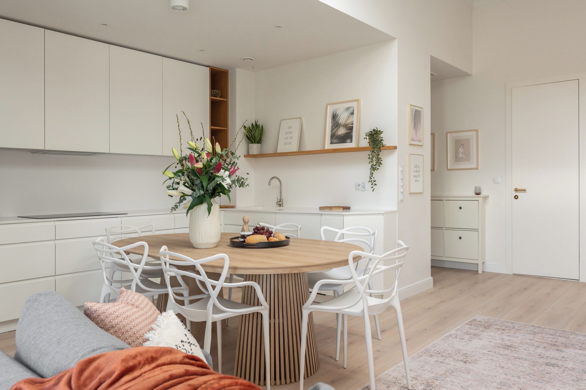 A modern kitchen with white cabinetry, a wooden dining table, and white chairs.