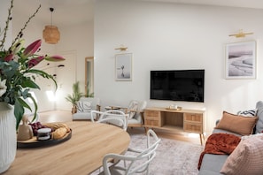 Ett modernt vardagsrum med ett matbord i trä, vita stolar, en soffa, en tv och konstverk på väggarna.